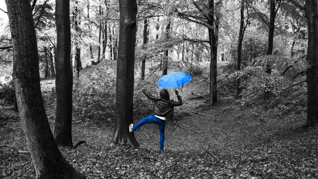 Black and white picture of woodland with person dancing with blue umbrella