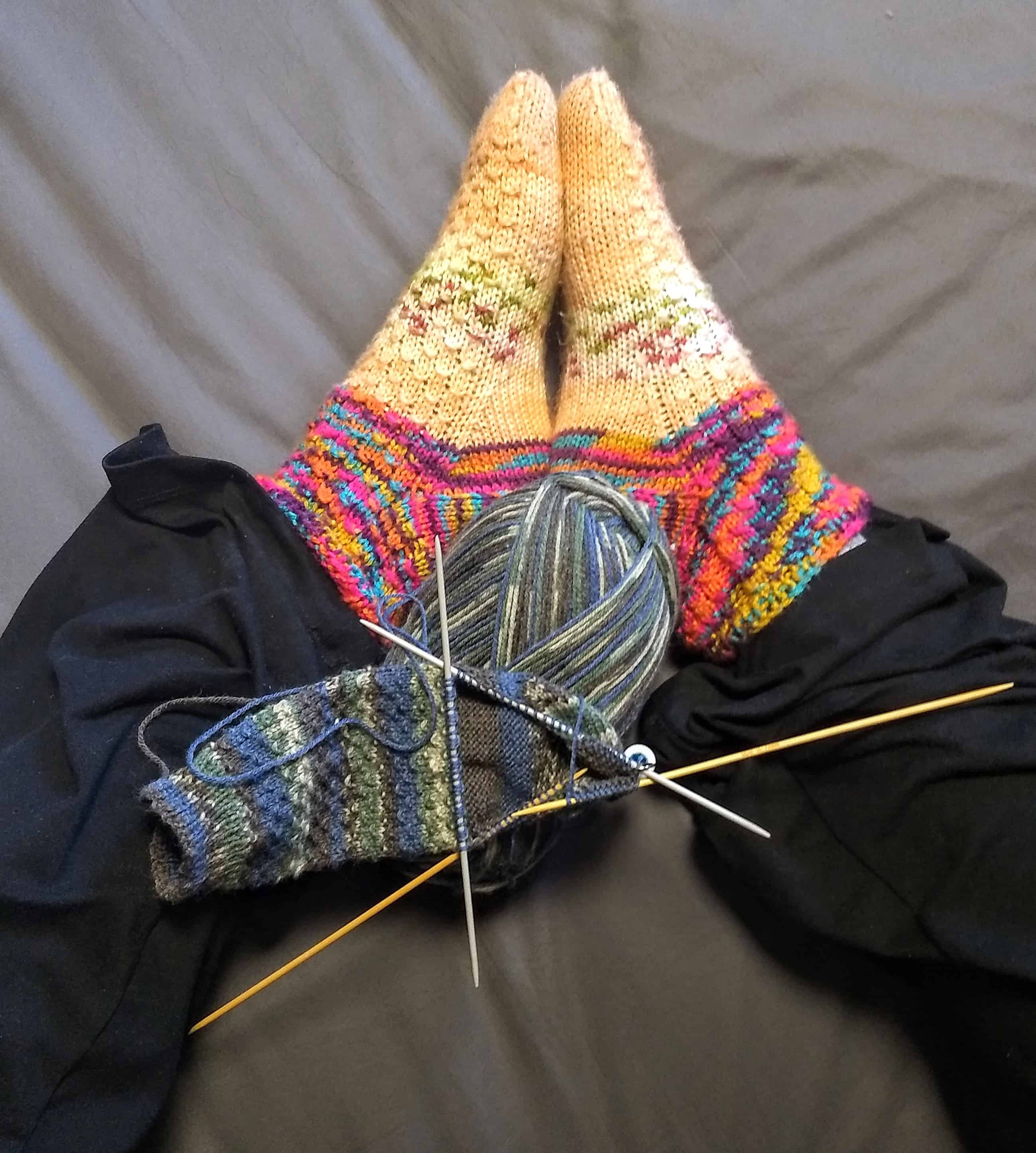 Picture of a person's knitting over feet covered in knitted socks.