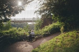 man sitting on bench in nature with Bristol Suspension Bridge in the background.