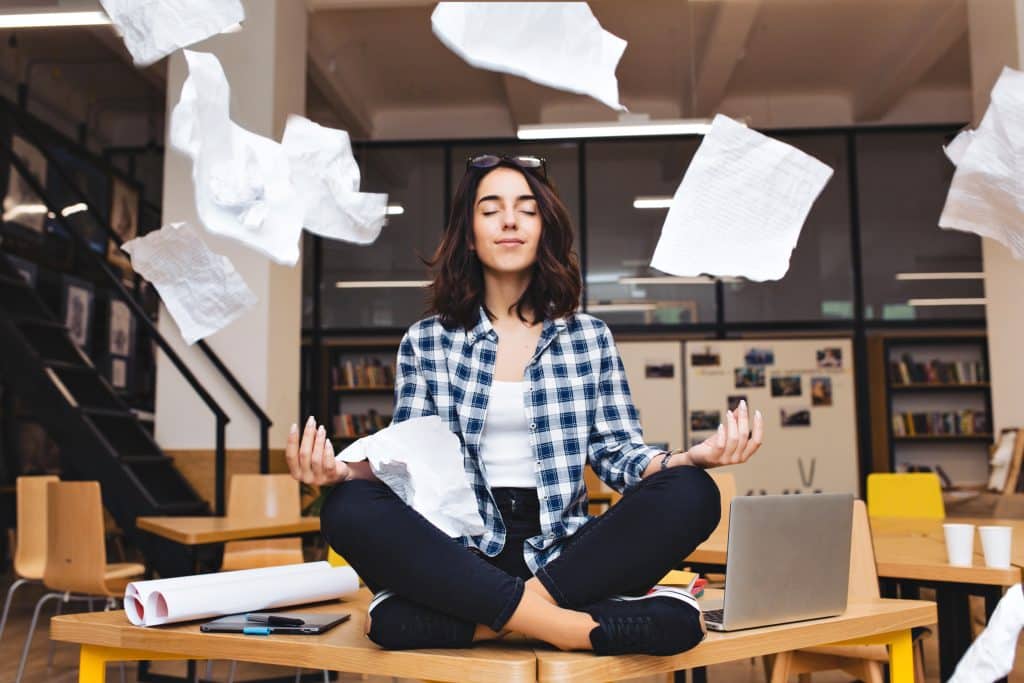 woman meditating on a table looking serene while papers fly around her.