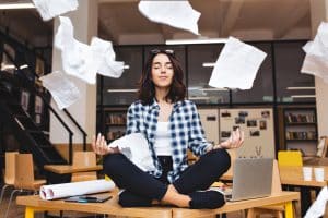 woman meditating on a table looking serene while papers fly around her.