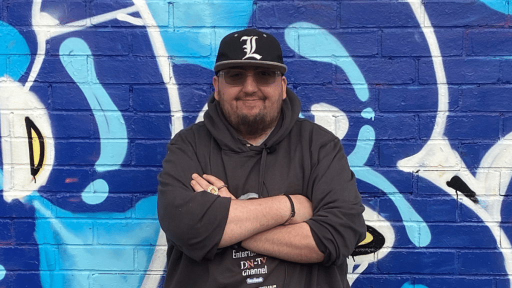 Drew standing arms crossed in front of a wall with colourful artwork on